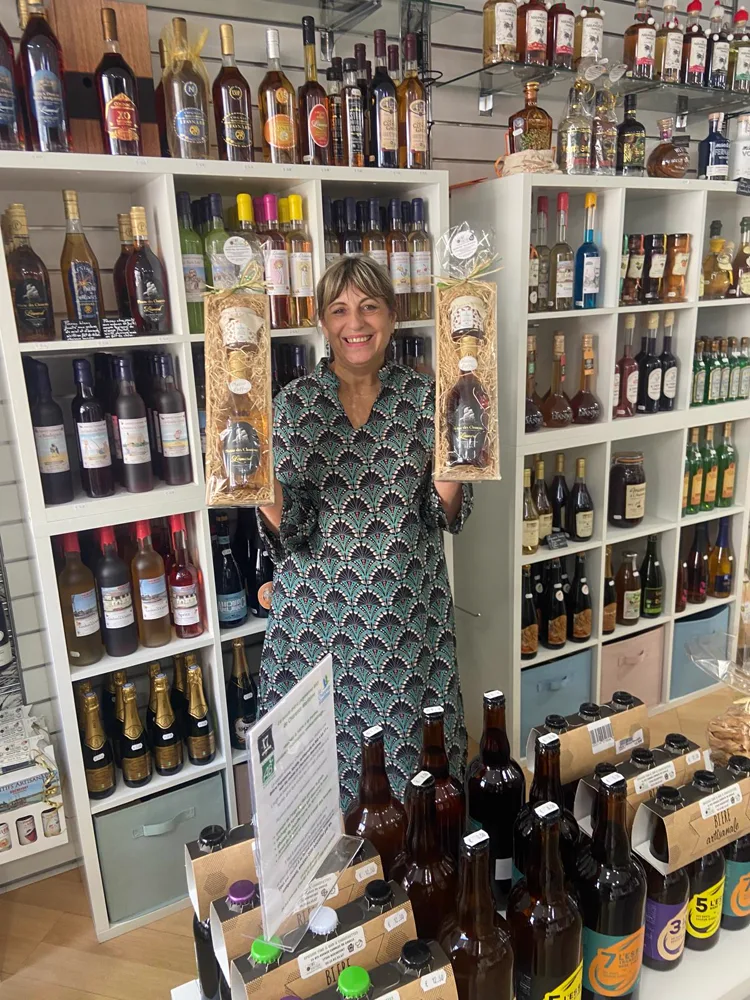Nathalie, du Café Boutique, tenant deux coffrets cadeaux devant les étagères de bouteilles de la boutique